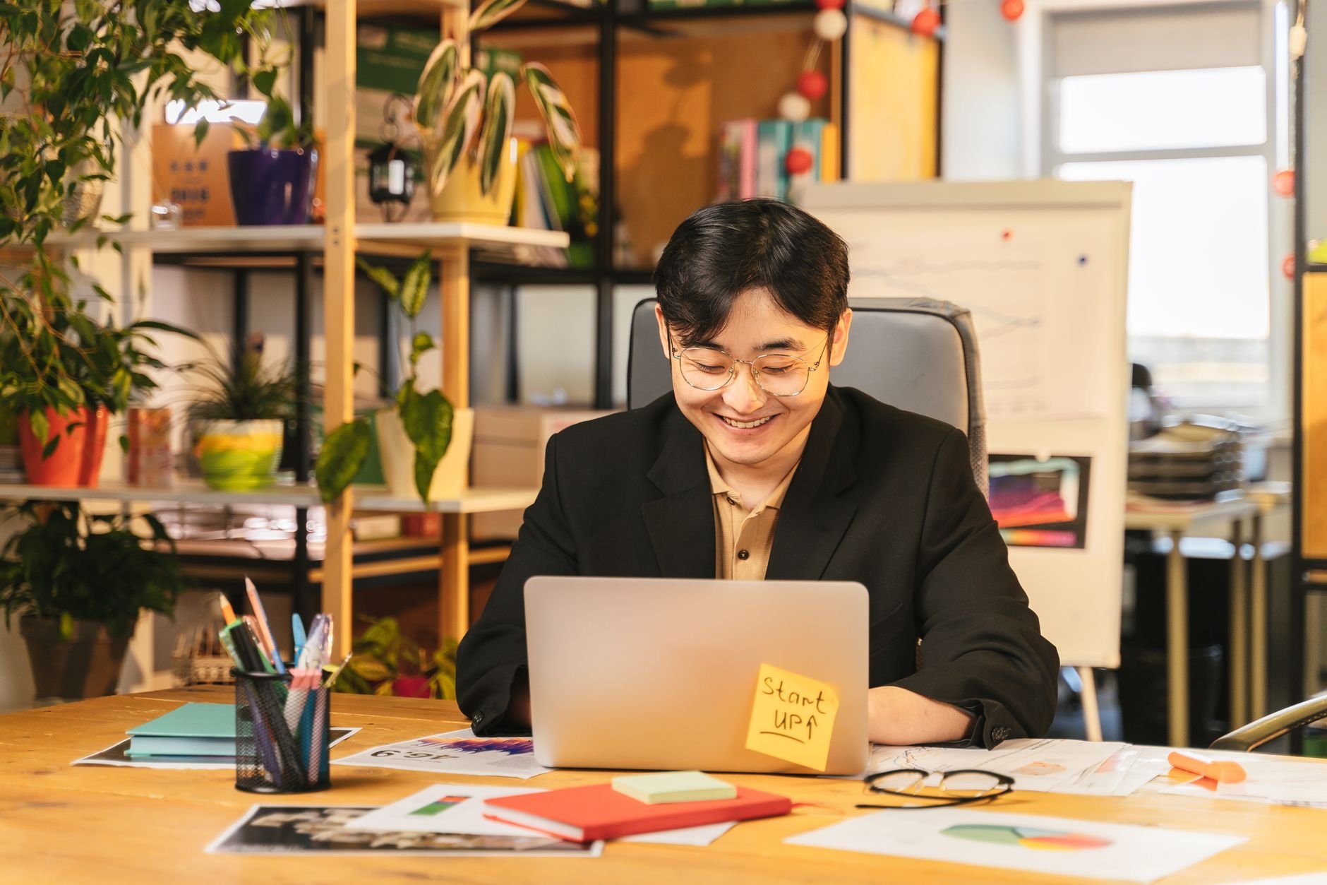 Smiling young professional working on a laptop at a cozy desk surrounded by plants